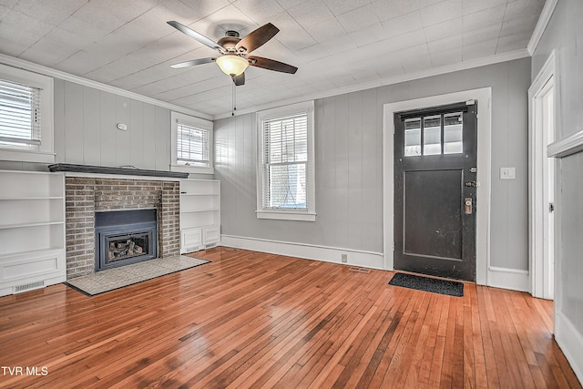 foyer entrance with ornamental molding, a brick fireplace, wood-type flooring, and ceiling fan