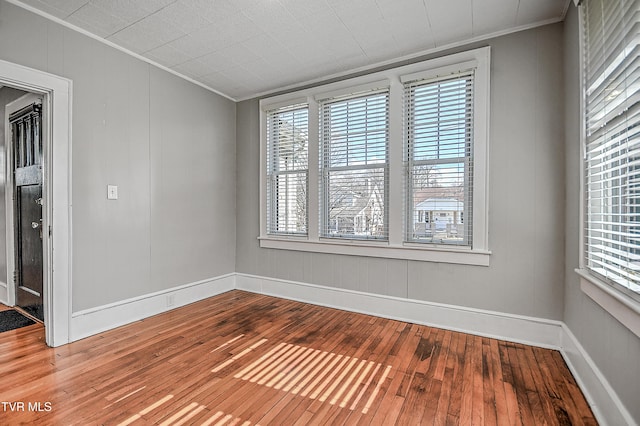 empty room with hardwood / wood-style flooring, ornamental molding, and plenty of natural light