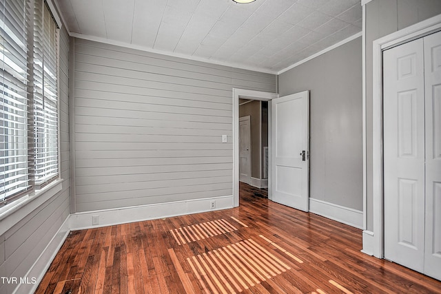 unfurnished bedroom with crown molding, dark wood-type flooring, wooden walls, and a closet