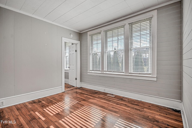 empty room with plenty of natural light, wooden walls, and hardwood / wood-style floors