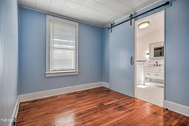 unfurnished bedroom featuring hardwood / wood-style flooring, ensuite bath, and a barn door