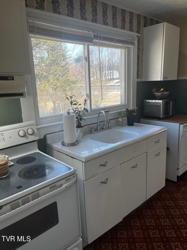 kitchen featuring white cabinetry, sink, white appliances, and a healthy amount of sunlight