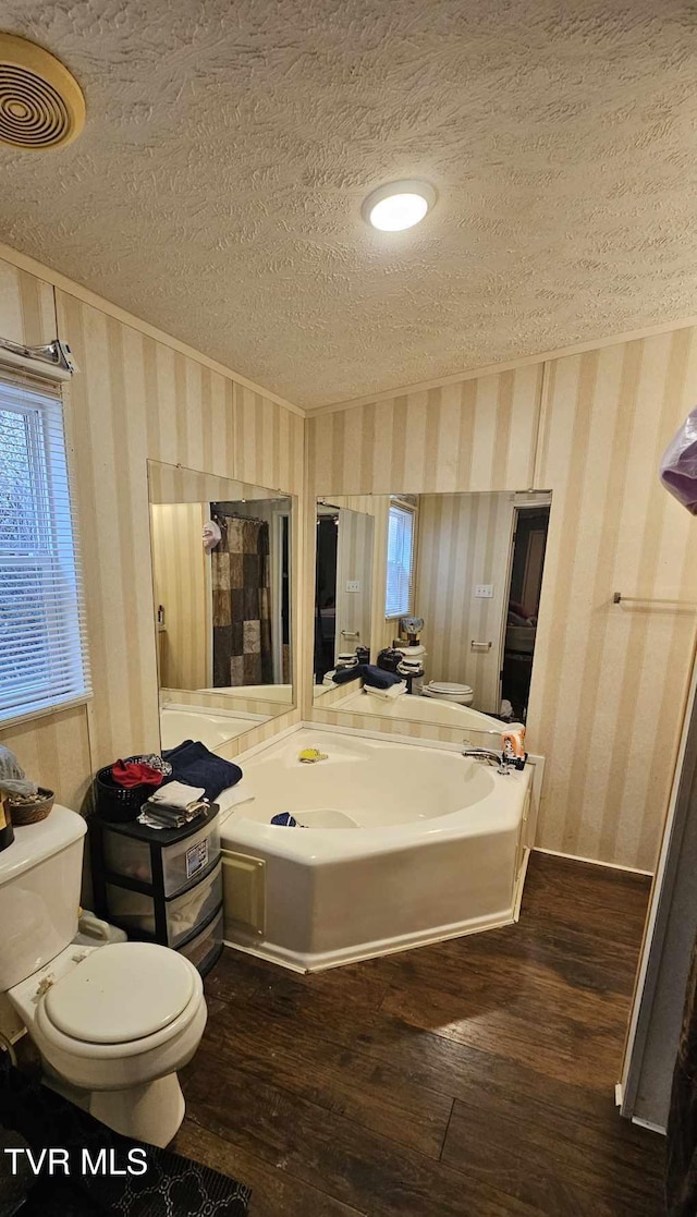 bathroom with toilet, hardwood / wood-style floors, a textured ceiling, and a washtub