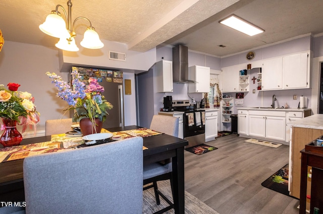 kitchen featuring decorative light fixtures, white cabinets, wood-type flooring, appliances with stainless steel finishes, and wall chimney range hood