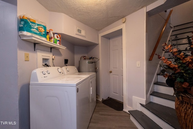 clothes washing area with washing machine and dryer, water heater, wood-type flooring, and a textured ceiling