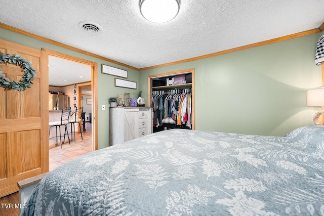 bedroom featuring crown molding, a textured ceiling, stainless steel refrigerator, and a closet