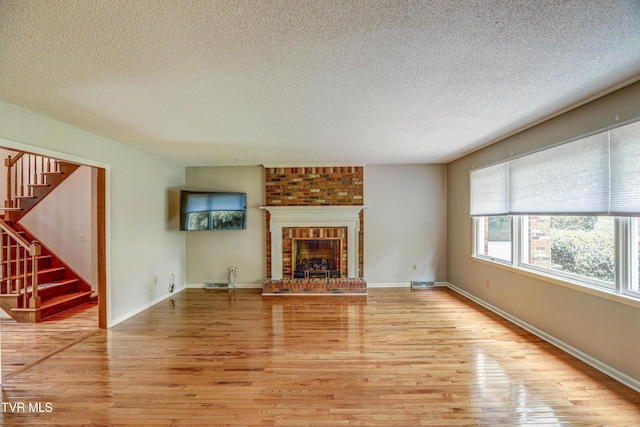 205 Donegal Way Unit 205, Bristol, TN 37620 - unfurnished living room with stairs, a textured ceiling, visible vents, light wood finished floors, and a brick fireplace
