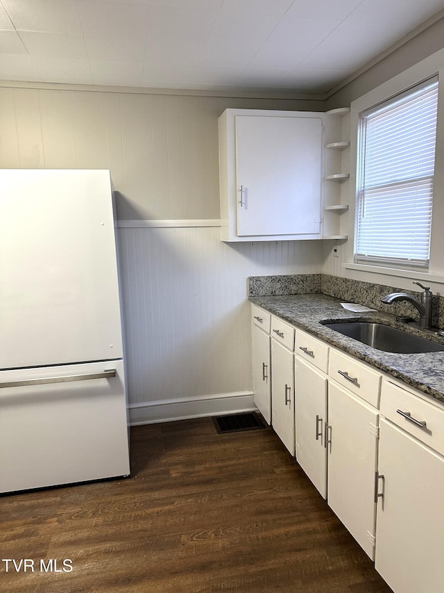 kitchen featuring dark wood finished floors, white cabinetry, freestanding refrigerator, and a sink