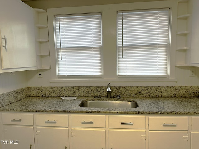 kitchen featuring a sink, open shelves, light stone countertops, and white cabinetry