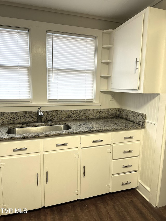 kitchen featuring dark wood finished floors, a wealth of natural light, dark stone countertops, white cabinets, and a sink