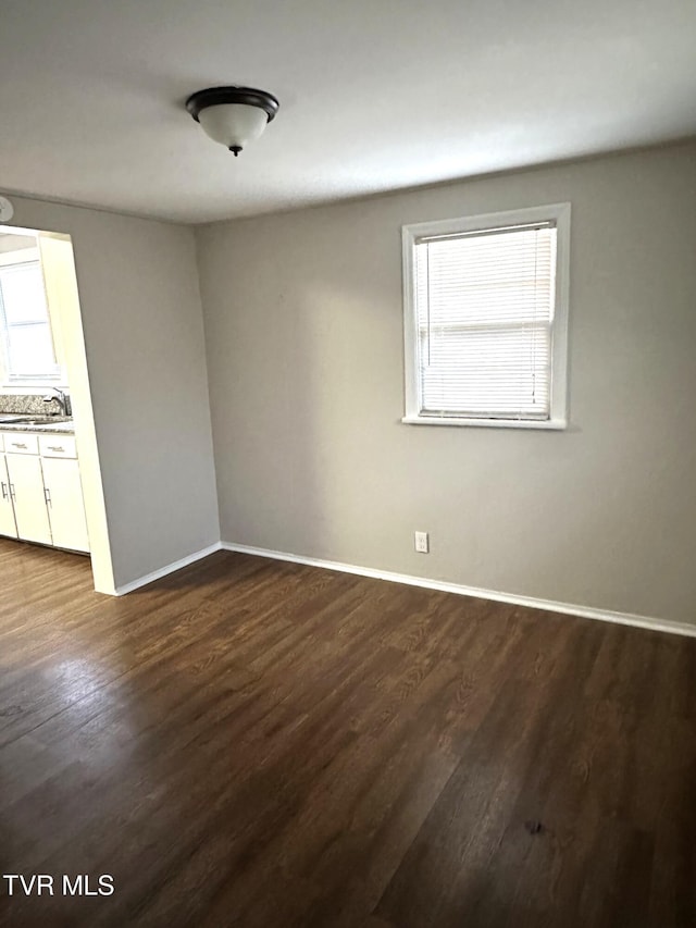 unfurnished room with a sink, baseboards, and dark wood-type flooring