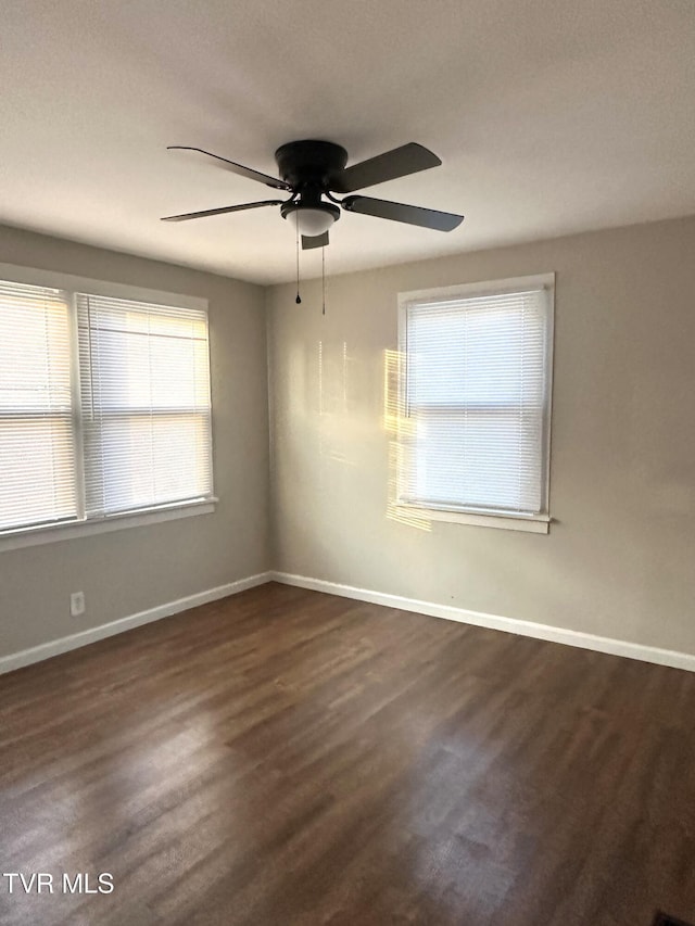 spare room featuring dark wood-style floors, a ceiling fan, and baseboards