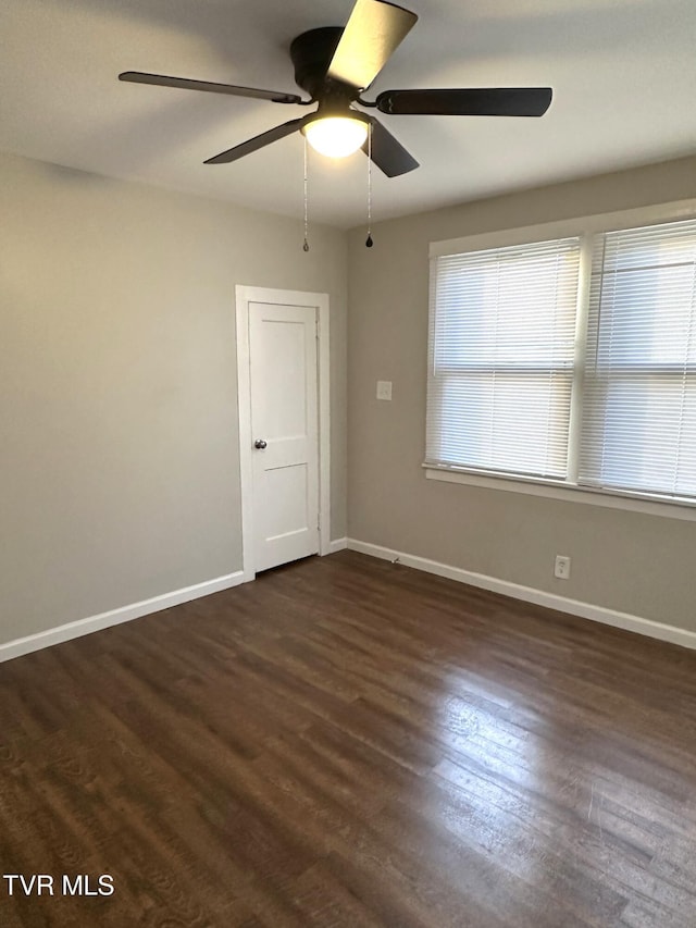 spare room featuring dark wood-type flooring, a ceiling fan, and baseboards