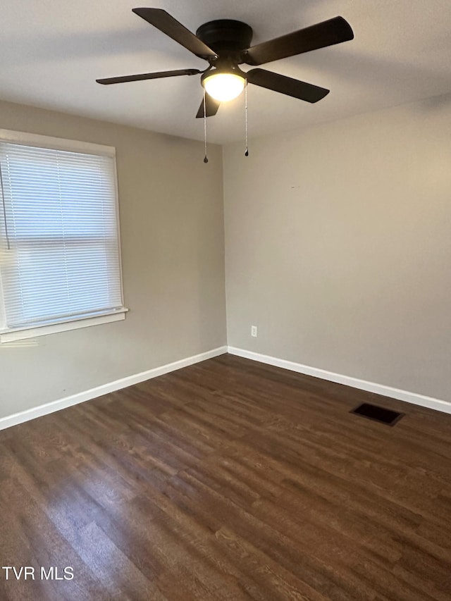 empty room featuring visible vents, a ceiling fan, dark wood-type flooring, and baseboards