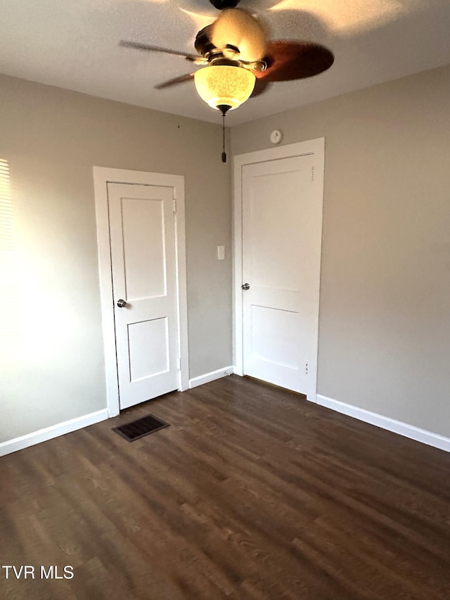 unfurnished bedroom featuring visible vents, baseboards, dark wood-type flooring, and a ceiling fan