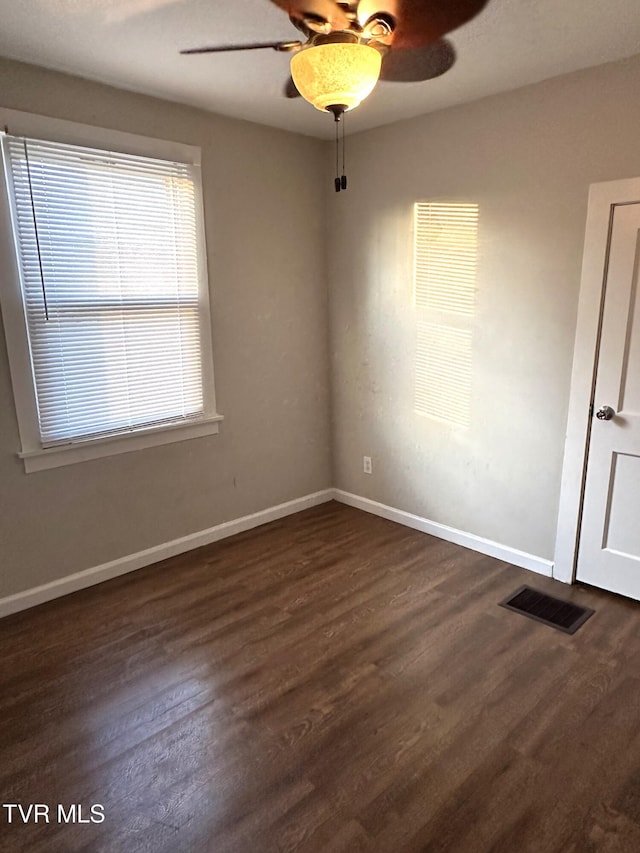 empty room with visible vents, baseboards, dark wood-type flooring, and a ceiling fan