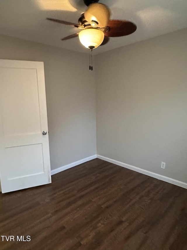 spare room with dark wood finished floors, a ceiling fan, and baseboards