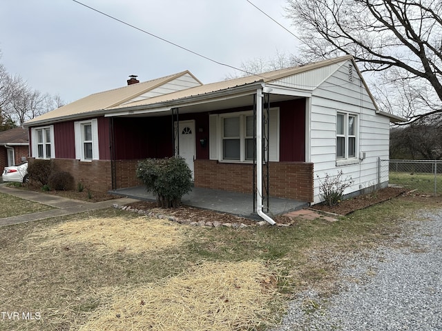 view of front of house featuring a porch, fence, brick siding, and metal roof