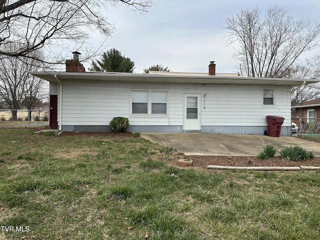 rear view of house featuring a lawn, a patio area, fence, and a chimney