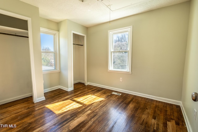 unfurnished bedroom featuring attic access, baseboards, visible vents, dark wood-style flooring, and multiple closets