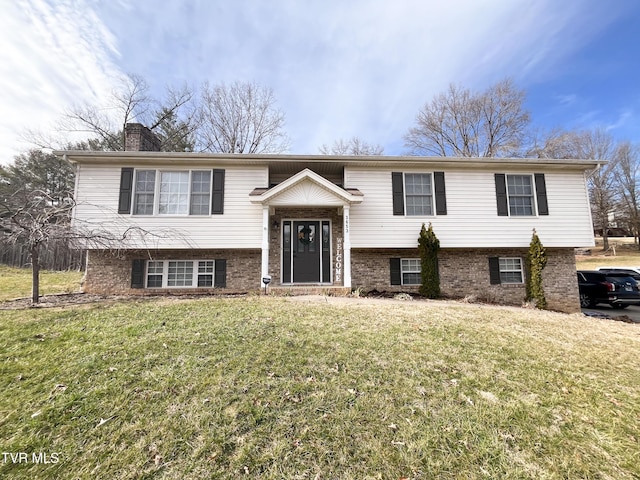 bi-level home with brick siding, a chimney, and a front yard