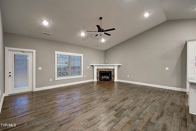 unfurnished living room featuring vaulted ceiling, a stone fireplace, dark hardwood / wood-style floors, and ceiling fan