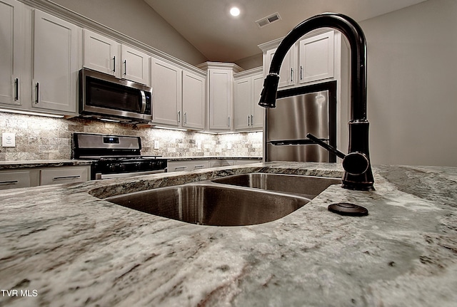 kitchen featuring white cabinetry, appliances with stainless steel finishes, light stone counters, and decorative backsplash