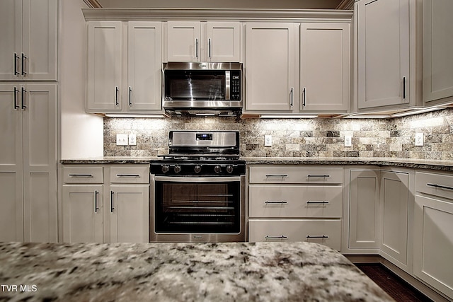 kitchen with light stone counters, decorative backsplash, stainless steel appliances, and white cabinets