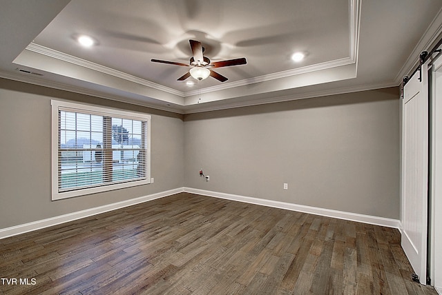 unfurnished bedroom featuring ornamental molding, a barn door, dark hardwood / wood-style flooring, and a tray ceiling