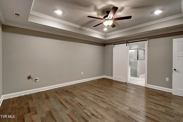 unfurnished bedroom featuring ornamental molding, a tray ceiling, a barn door, and dark hardwood / wood-style flooring