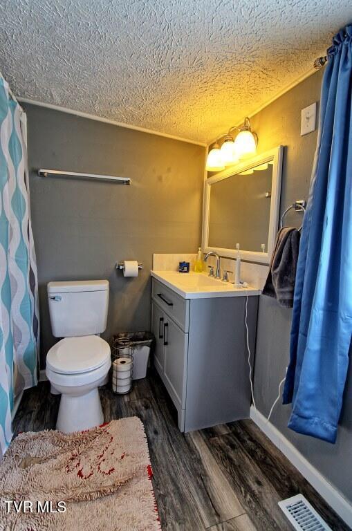 bathroom featuring vanity, wood-type flooring, toilet, and a textured ceiling