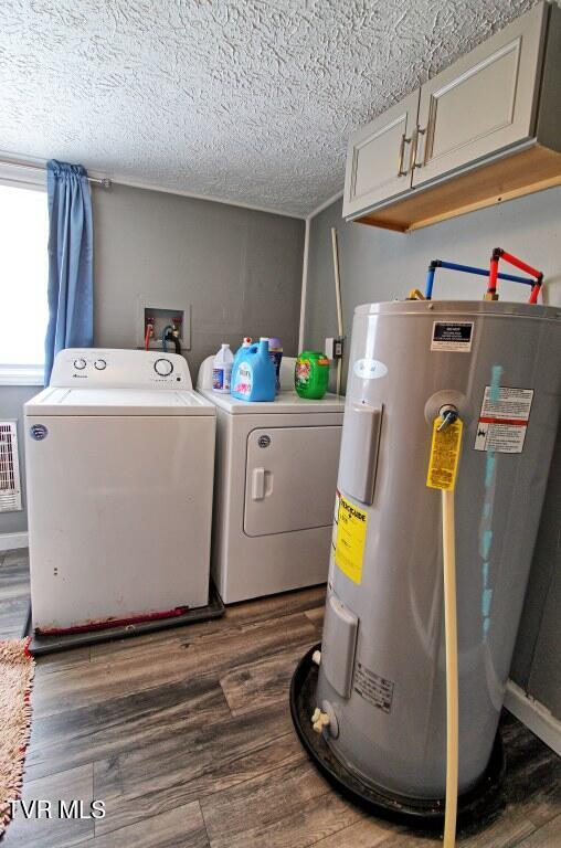 clothes washing area featuring washing machine and dryer, cabinets, electric water heater, a textured ceiling, and dark hardwood / wood-style flooring