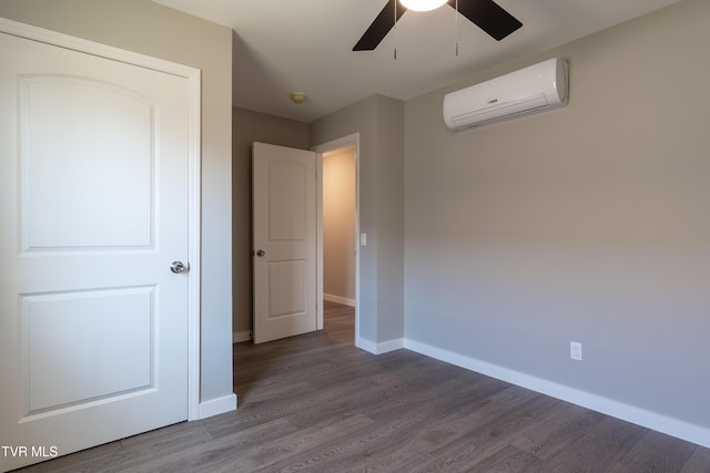 unfurnished bedroom with ceiling fan, baseboards, an AC wall unit, and wood finished floors