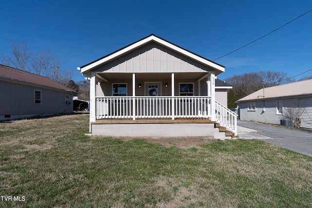 bungalow-style house with board and batten siding, covered porch, a front lawn, and central AC unit