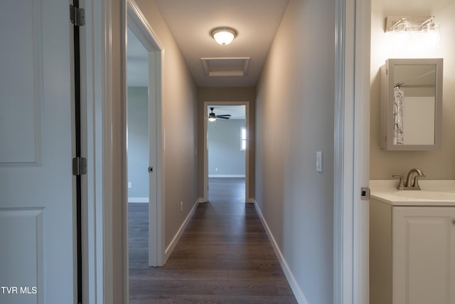 hallway with dark wood-style flooring, a sink, attic access, and baseboards