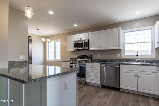 kitchen with stainless steel appliances, a peninsula, a sink, white cabinetry, and hanging light fixtures