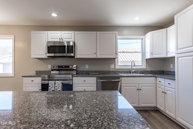 kitchen featuring appliances with stainless steel finishes, dark stone countertops, a sink, and white cabinets