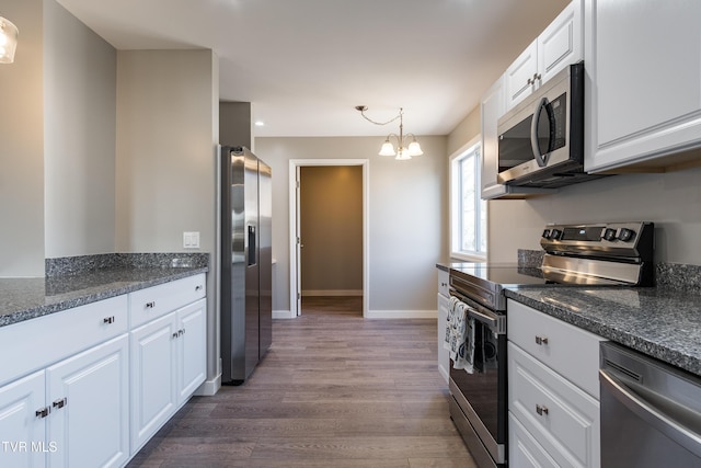 kitchen featuring stainless steel appliances, hanging light fixtures, white cabinets, wood finished floors, and baseboards