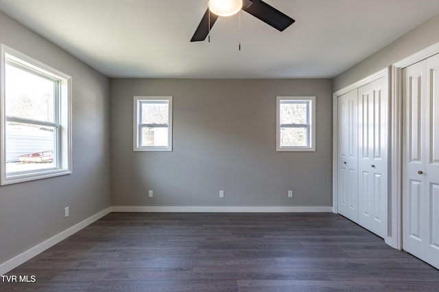 unfurnished bedroom with multiple windows, dark wood finished floors, baseboards, and two closets