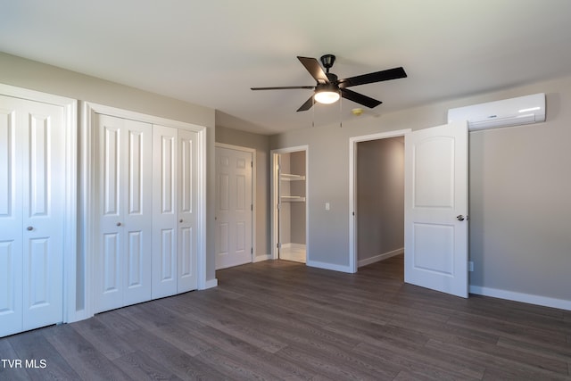 unfurnished bedroom with baseboards, dark wood finished floors, a wall unit AC, ceiling fan, and multiple closets