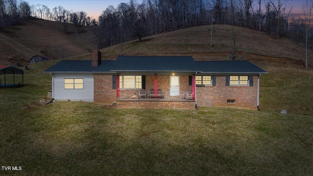 view of front of house featuring covered porch, brick siding, a yard, and a chimney