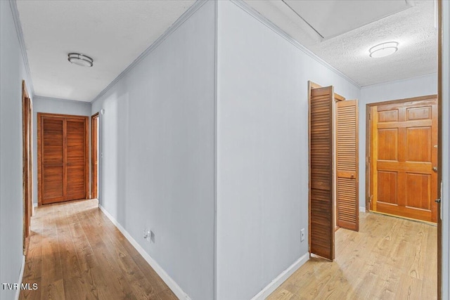 hall with light wood finished floors, baseboards, ornamental molding, and a textured ceiling