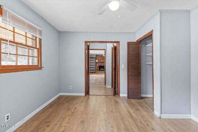 unfurnished room featuring ornamental molding, a brick fireplace, light wood-style flooring, and a ceiling fan