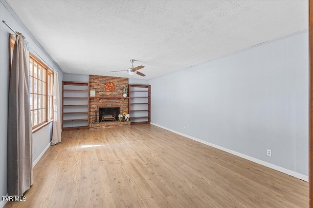 unfurnished living room with a ceiling fan, light wood-style flooring, a textured ceiling, a brick fireplace, and built in shelves