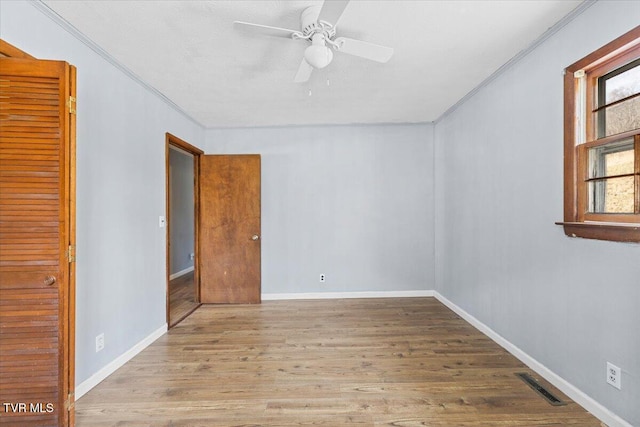 empty room with crown molding, visible vents, a ceiling fan, light wood-type flooring, and baseboards