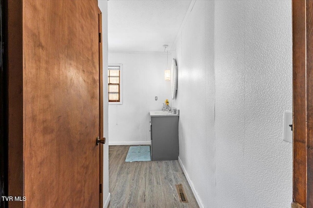 bathroom with a textured ceiling, a textured wall, wood finished floors, vanity, and baseboards