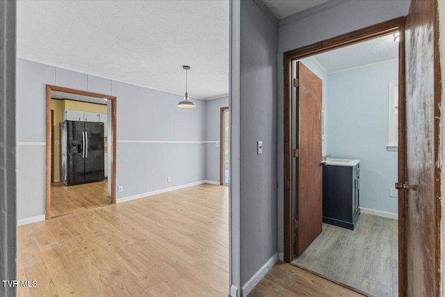 corridor featuring baseboards, crown molding, a textured ceiling, and light wood finished floors