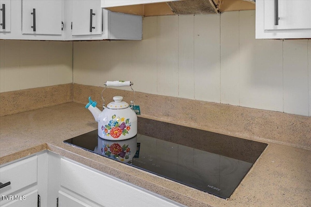 kitchen featuring black electric stovetop, range hood, white cabinetry, and light countertops