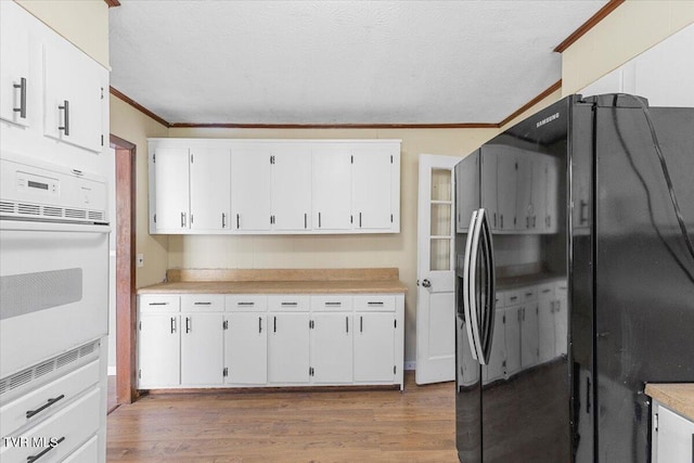 kitchen featuring oven, white cabinetry, light countertops, and freestanding refrigerator