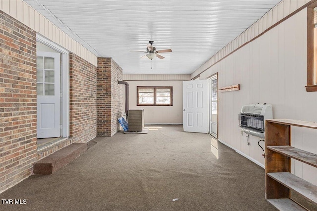 unfurnished living room with a ceiling fan, brick wall, heating unit, a wood stove, and dark colored carpet